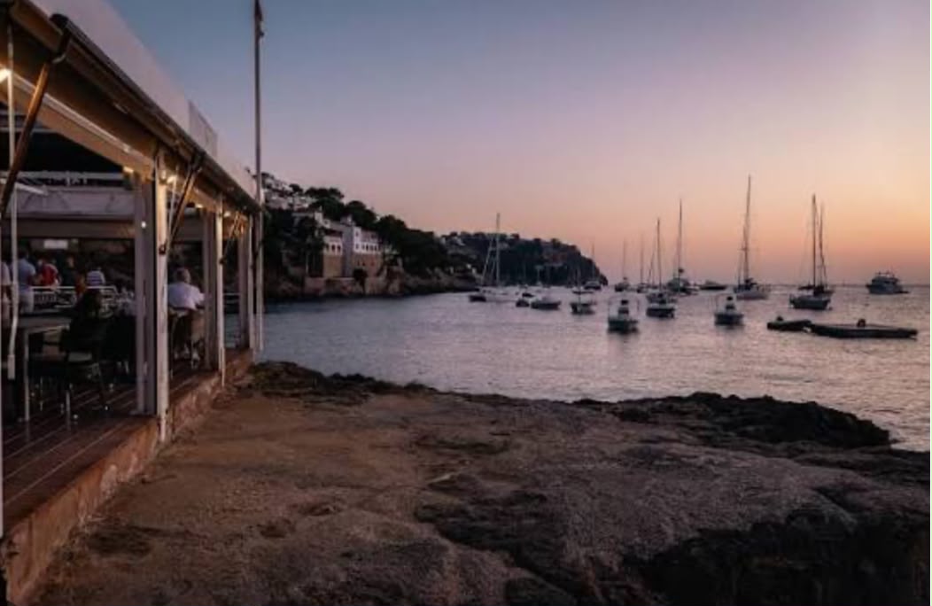 Terraza de Rocamar sobre el Puerto de Andratx al atardecer, con veleros fondeados en la bahía.