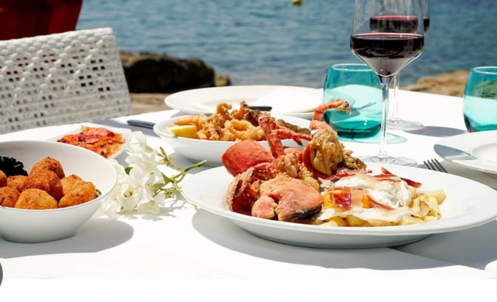 Marisco fresco de Rocamar servido junto al mar, con croquetas y una copa de vino.